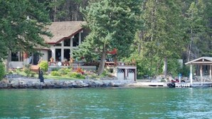 Un chalet au bord du lac, doté d’une grande terrasse et entouré d’une forêt dense.
