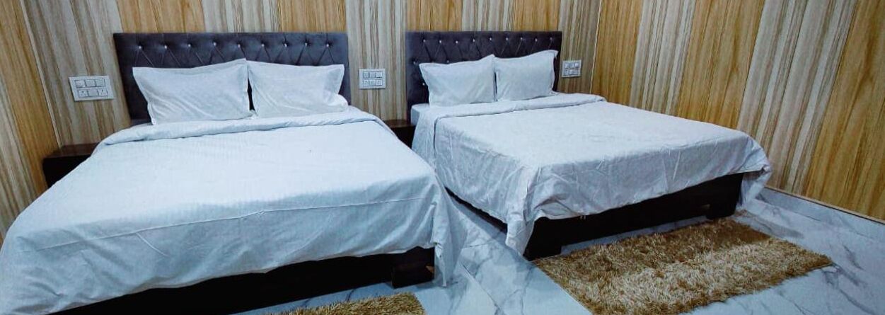 Dos camas individuales con sábanas blancas, cabecero oscuro y pared de madera con rayas verticales.