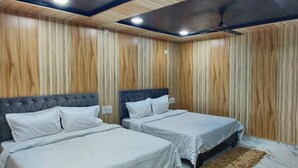 A bedroom with two beds, wooden panel walls, and a ceiling fan. - Hotel Ganga Sagar (Bhatwari)