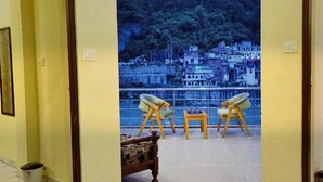 A room with a balcony, two chairs, a small table, and a view of a hillside. - Hotel Ganga Sagar (Bhatwari)