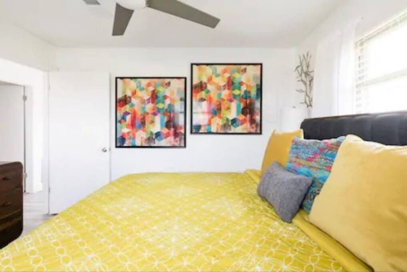 A bedroom with a yellow patterned bedspread, a black headboard, and two abstract paintings on the wall.