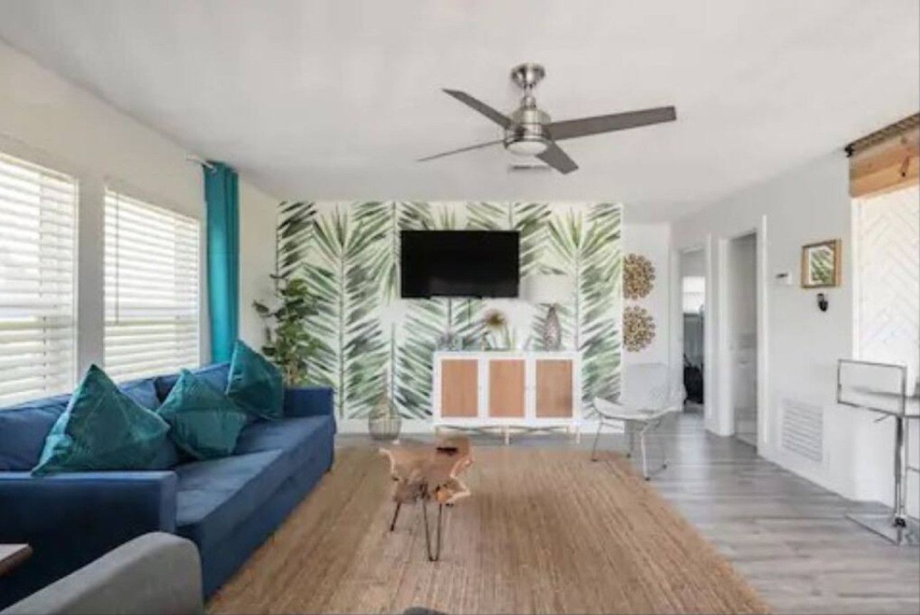 A modern living room with a blue sofa, a ceiling fan, and a wall-mounted TV.