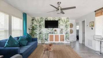 A modern living room with a blue sofa, a ceiling fan, and a wall-mounted TV.