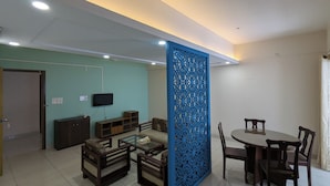 A living room with a TV, sofa, coffee table, and a dining area with chairs and a table. - YMCA Training Center and Guest House  (Savar)