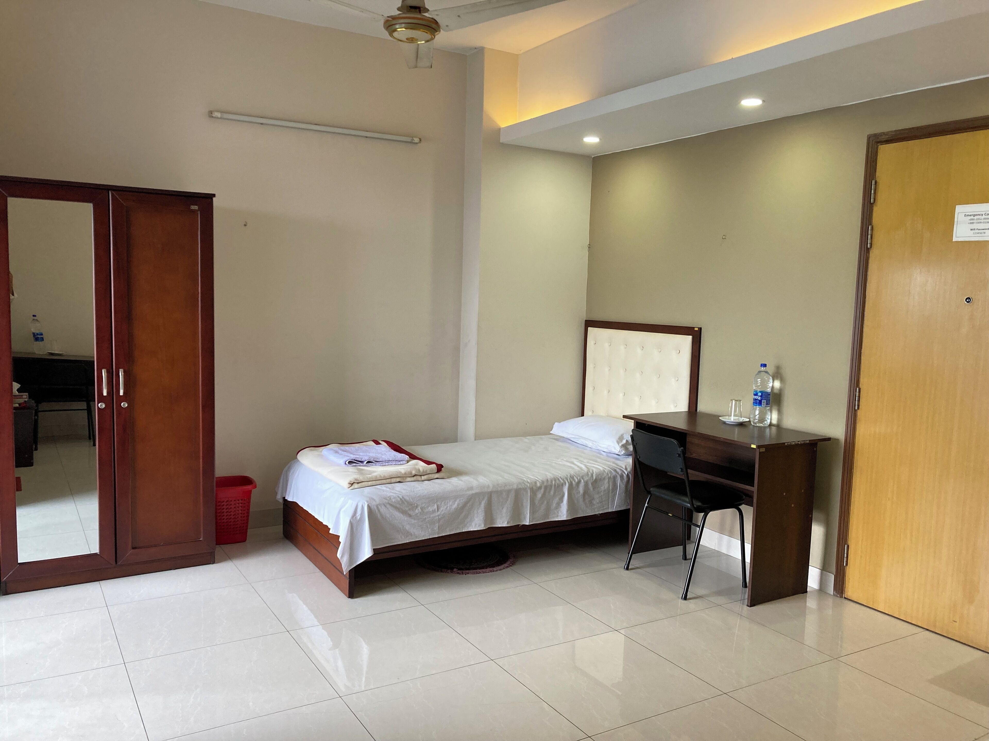 A hotel room with a bed, a desk, a chair, a wardrobe, and a door.