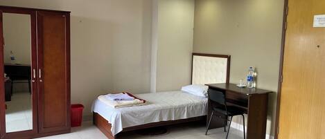A hotel room with a bed, a desk, a chair, a wardrobe, and a door.