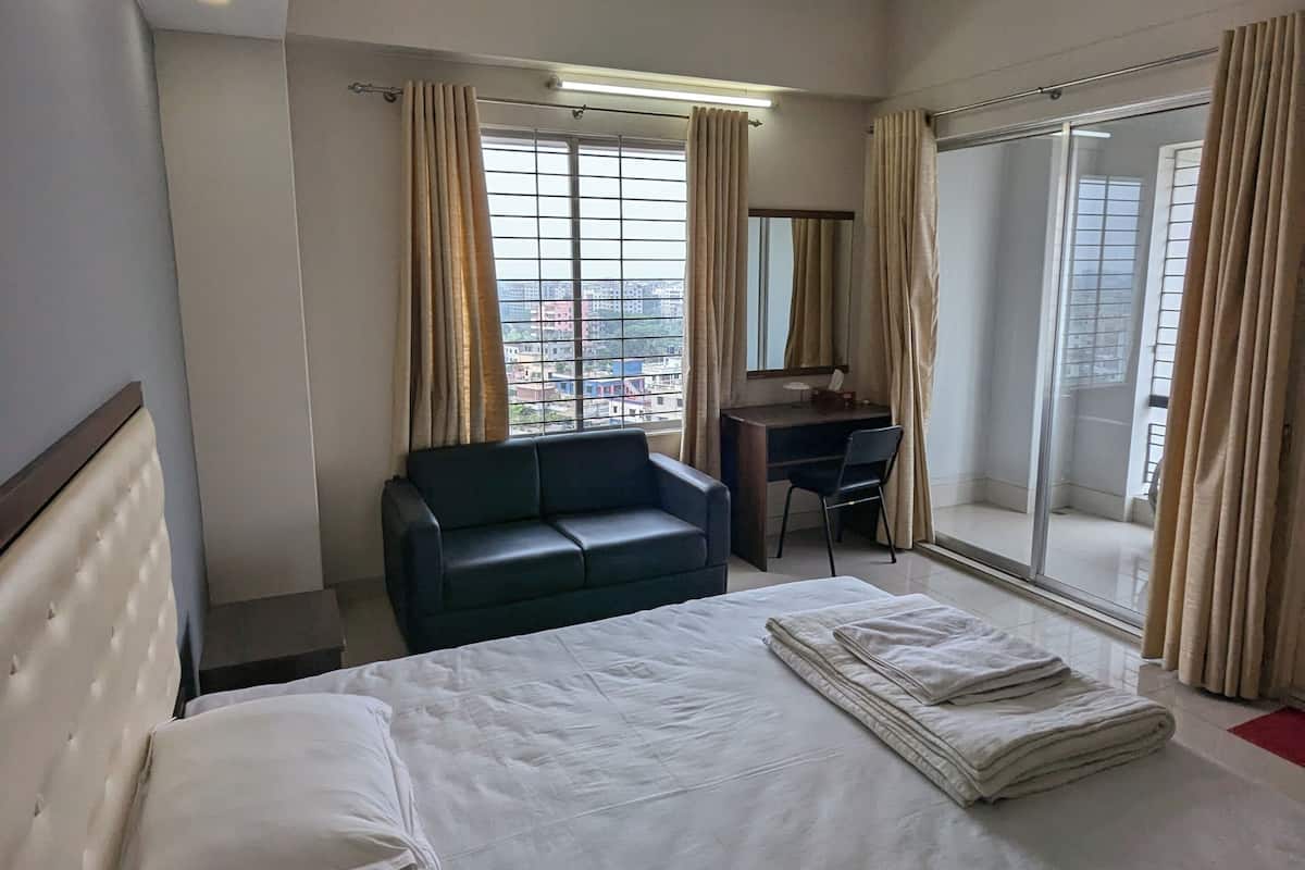 A hotel room with a bed, a desk, a chair, a sofa, and a view of the city.