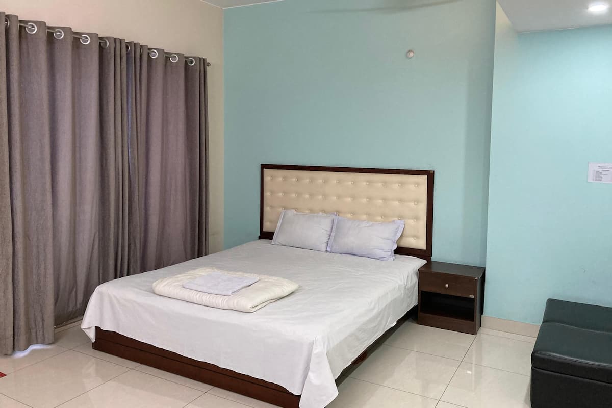 A neatly made bed with a white bedspread and pillows, a wooden headboard, a nightstand, and a dark-colored bench.