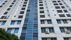 A high-rise building with a central glass facade, multiple air conditioning units, and a symmetrical window pattern. - YMCA Training Center and Guest House  (Savar)