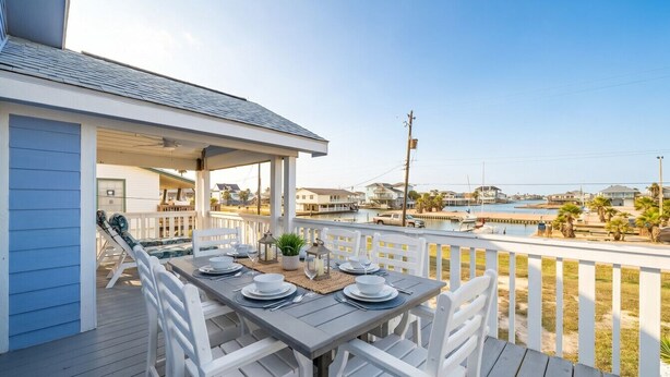 Un espace ext érieur abrité, aménagé pour les repas, avec une table pour quatre personnes, offrant une vue sur un port de plaisance et une plage.