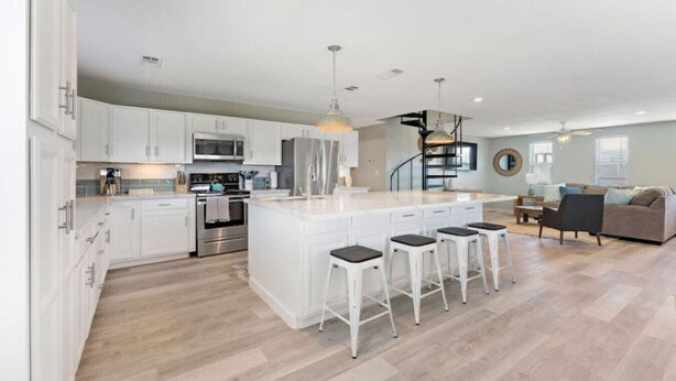 A modern kitchen with white cabinetry, stainless steel appliances, and a central island with bar stools. - Cozy Beach House with Game Room, Near the Beach (Crystal Beach)