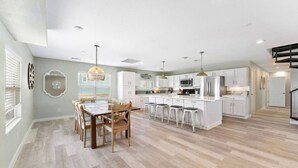 A spacious kitchen with white cabinets, a central island with bar stools, and pendant lighting. - Cozy Beach House with Game Room, Near the Beach (Crystal Beach)