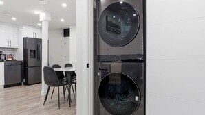 A modern kitchen with a built-in washer and dryer, a dining area with chairs, and a visible refrigerator.