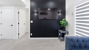 A modern interior with a flat-screen TV mounted on a black panel, a potted plant, a blue upholstered chair, and a white door.