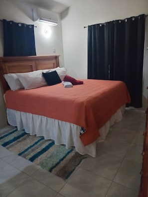 A bed with a headboard, a white pillow, a red pillow, and a folded white towel.