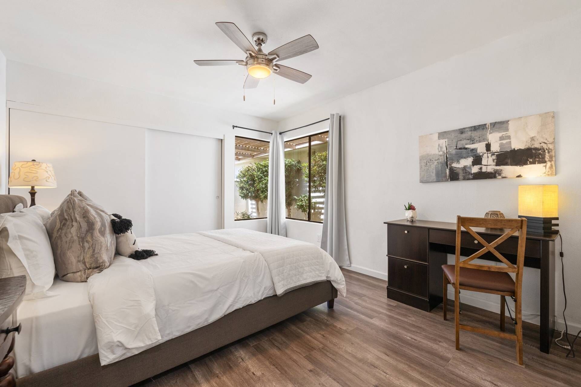 A bedroom with a bed, a desk, a chair, a ceiling fan, and a window with curtains.