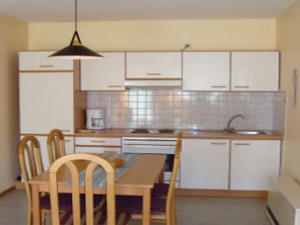 A compact kitchen with white cabinets, a wooden dining table, and chairs.