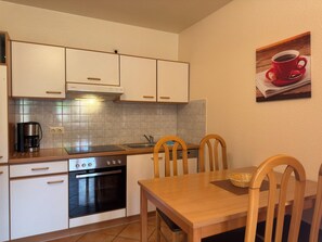 Cozinha compacta com armários brancos, forno embutido, cafeteira e mesa de jantar com cadeiras.