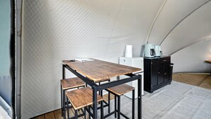 Un petit espace clos, avec une table et des bancs en bois, un réfrigérateur blanc et un meuble noir contenant une machine à café.