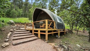 Une tente en forme de dôme dotée d’une terrasse en bois et d’un seul fauteuil Adirondack.