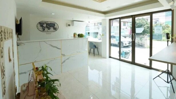 A modern hotel lobby with a marble reception desk, a world map decoration, a large window offering a view of the street, and a seating area with a chair. - Cozy Double Stay | Near Suvarnabhumi Airport Hub (Bangkok)