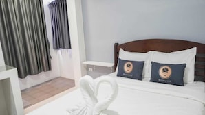 A hotel room with a bed, two pillows with a logo, a nightstand, a wooden headboard, and a window with curtains. - Cozy Double Stay | Near Suvarnabhumi Airport Hub (Bangkok)
