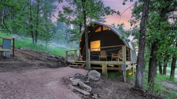 A rustic wooden cabin with a large open front door, surrounded by trees and a gravel path. - Escape to Cloud Nine Glamping in the Black Hills (Hermosa)