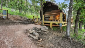 A dome-shaped cabin with a wooden deck and a chair, surrounded by trees and a gravel path. - Escape to Cloud Nine Glamping in the Black Hills (Hermosa)