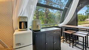 A kitchenette with a coffee maker and a small refrigerator, a dark wooden cabinet, and a table with two stools. - Escape to Cloud Nine Glamping in the Black Hills (Hermosa)