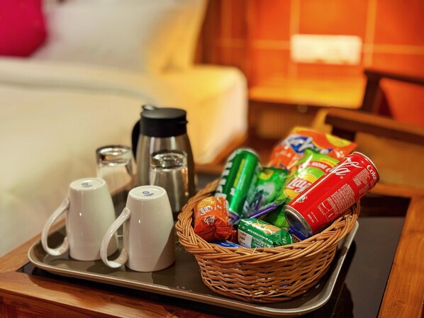 A tray with a basket of snacks, a thermos, and two mugs on a wooden table in a hotel room. - Leopard Hill Resort - Bandipur (Gundlupet)