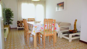 A dining area with a table and chairs, a sofa, a small table with a bowl, and a plant. - Apartment in Porto Santa Margherita (Porto Santa Margherita)