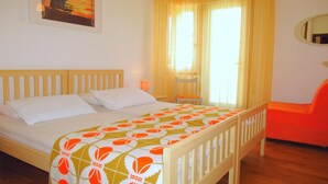 A bedroom with a wooden bed, a nightstand, a chair, a window with curtains, and a wall-mounted mirror. - Apartment in Porto Santa Margherita (Porto Santa Margherita)