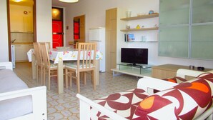 A compact living space with a dining area, a sofa, a television, and a kitchen area. - Apartment in Porto Santa Margherita (Porto Santa Margherita)