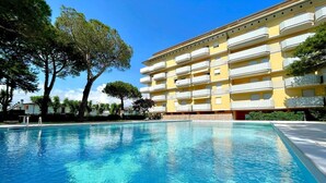 A swimming pool with a yellow building in the background. - Apartment in Porto Santa Margherita (Porto Santa Margherita)