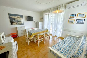 Una habitación con cama, una mesa y sillas, lavadora, televisor y refrigerador.