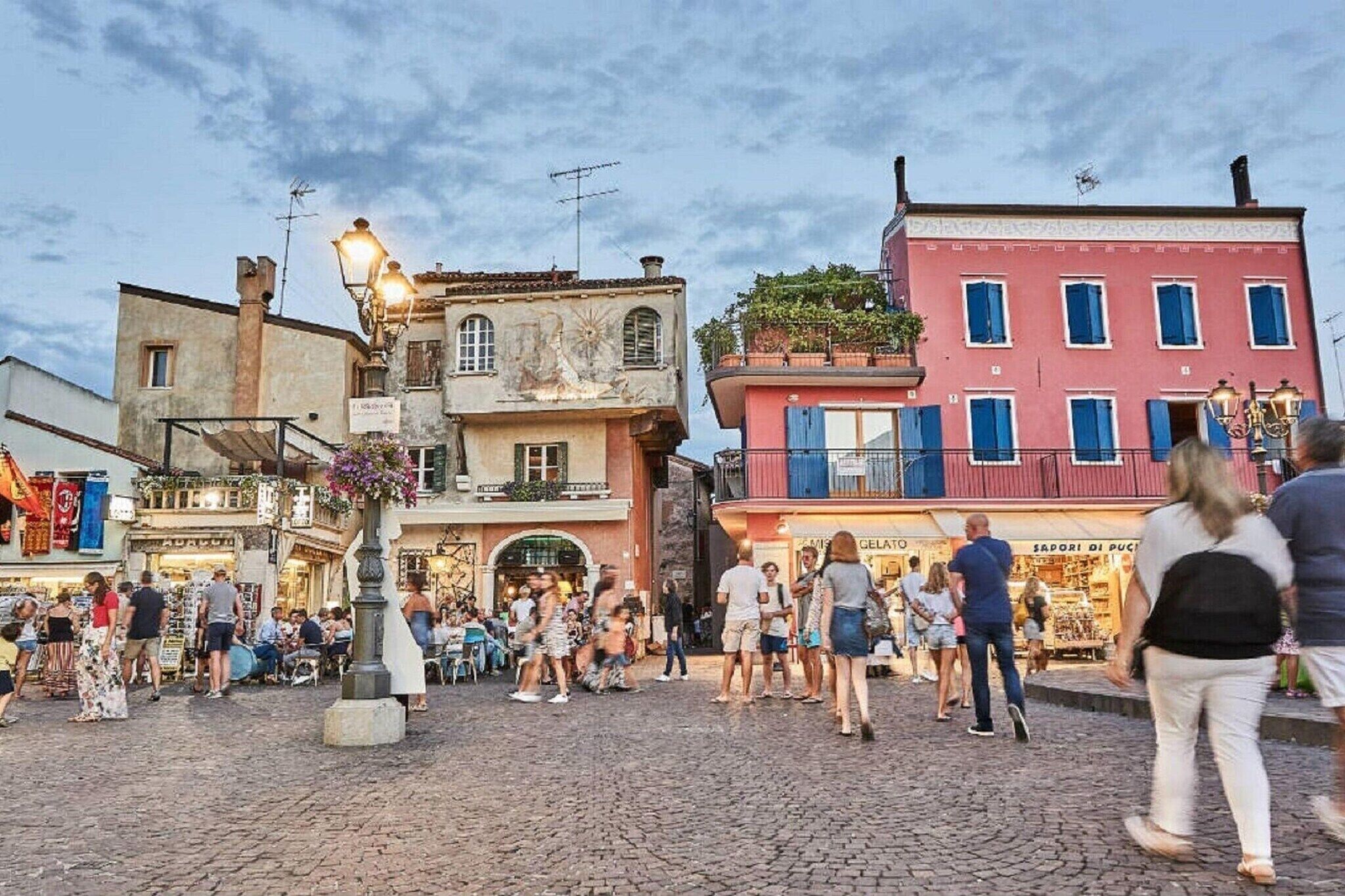 Uma praça de paralelepípedos com edifícios históricos, mesas ao ar livre e diversas lojas.