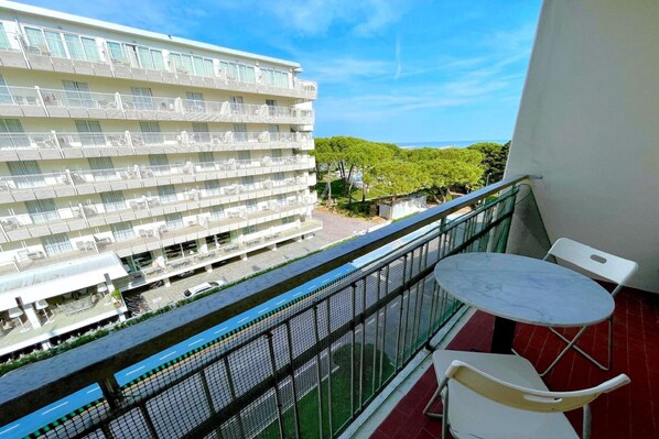 A balcony with a table and chairs, overlooking a modern building with multiple balconies and a view of the sea.