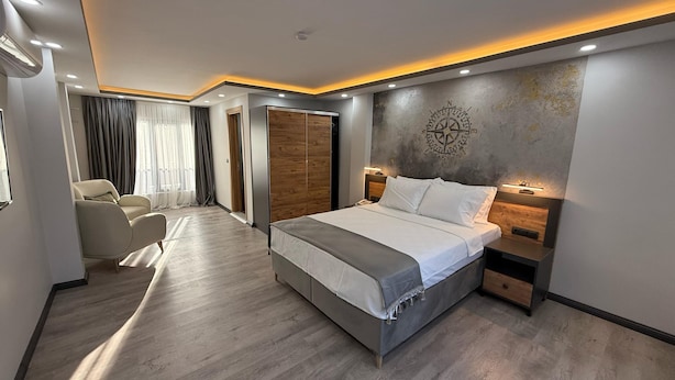A modern hotel room with a large bed, a seating area with a chair, and a wooden wardrobe. - Zeus Otel (Kusadasi)