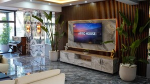 A modern living room with a large flat-screen TV, marble flooring, and potted plants. - Zeus Otel (Kusadasi)