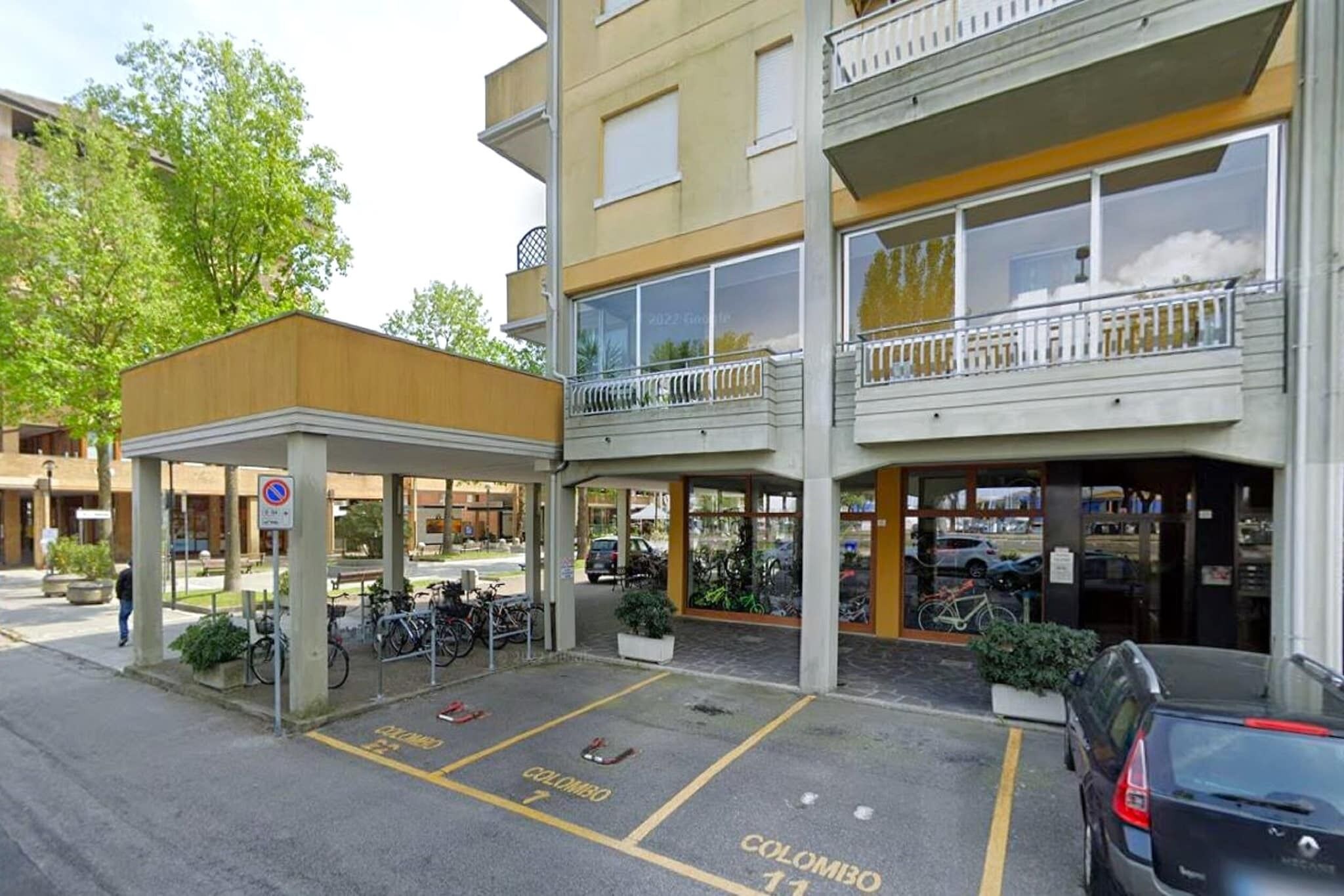 A multi-story building with a covered entrance, outdoor parking with marked spaces, and a sign indicating a no parking zone.