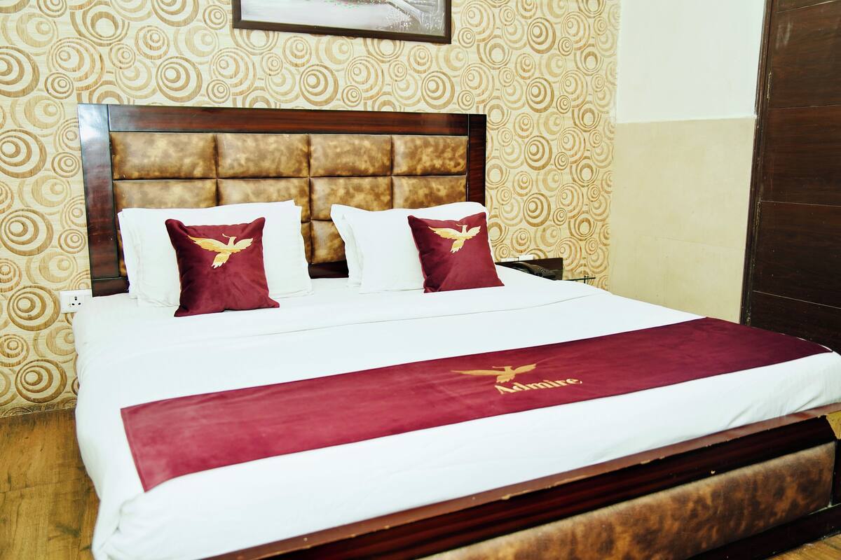 Una cama bien hecha con una colcha y almohadas color burdeos, un cabecero de madera y papel tapiz estampado.