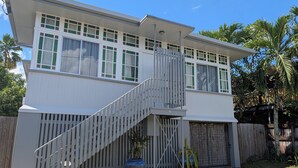 Une maison à deux étages, avec une façade blanche, un porche abrité et un escalier menant au deuxième étage.