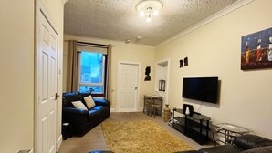 A living room with a black leather sofa, a TV, and a small table with a vase.