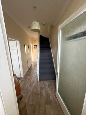 Een gang met een houten vloer, een deur met glas-in-lood, een trap en een hangende lamp.