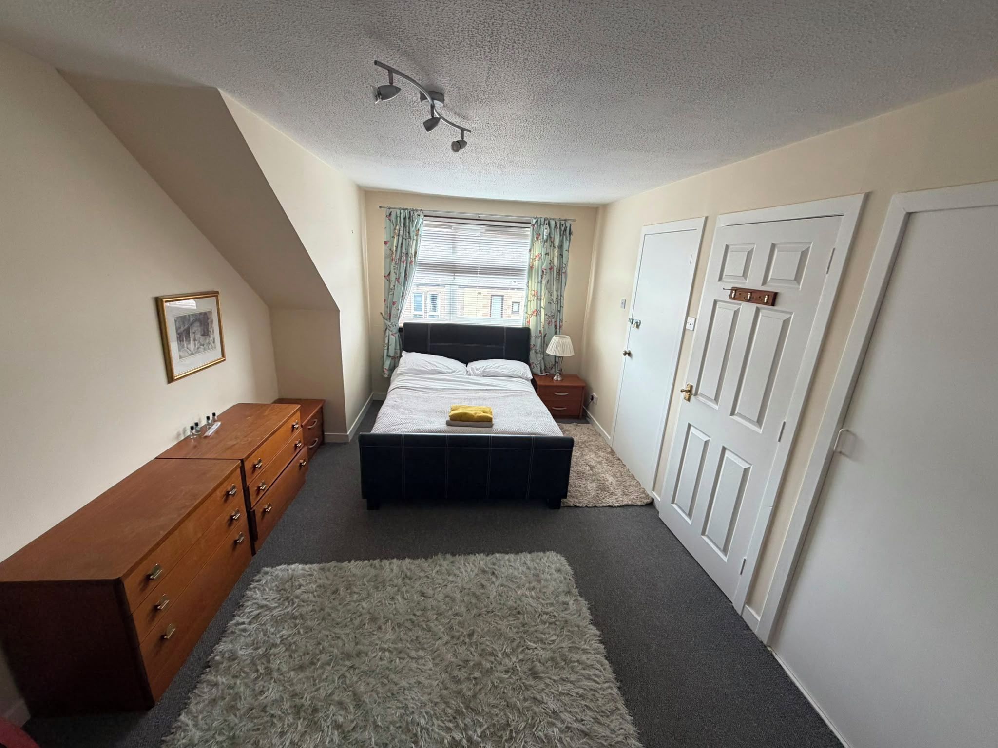 Une chambre à coucher avec un lit, une commode, une table de chevet et une porte.