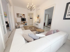 A modern living room with a large white sofa, a chandelier, and a TV.
