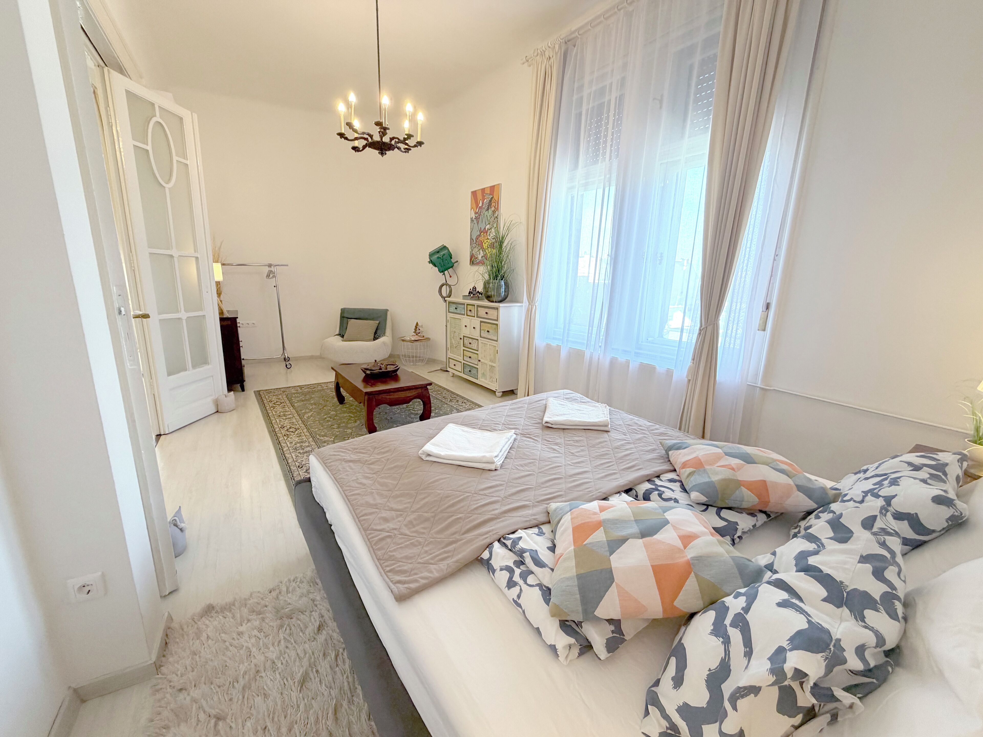 Un dormitorio con cama, una silla, un escritorio, una lámpara y una ventana con cortinas.