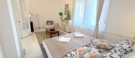 Un dormitorio con cama, una silla, un escritorio, una lámpara y una ventana con cortinas.