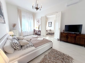 A modern bedroom with a large bed, a television, and a view into the living area.
