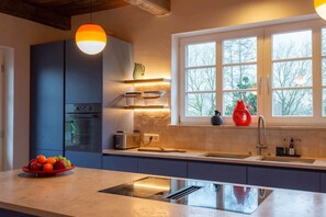 A modern kitchen with a built-in oven, a sink, and a window with a view of trees. - NEW: HackmannsHof. Half-timbered courtyard in the countryside. (Ankum)
